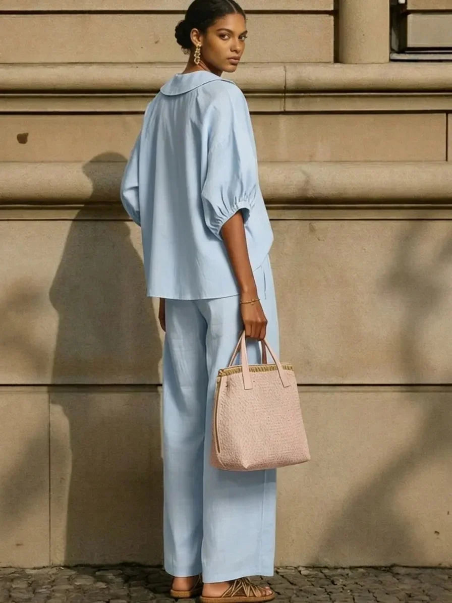 Woman in light blue relaxed fit blouse and wide-leg pants, holding pink woven tote, stylish plus size outfit