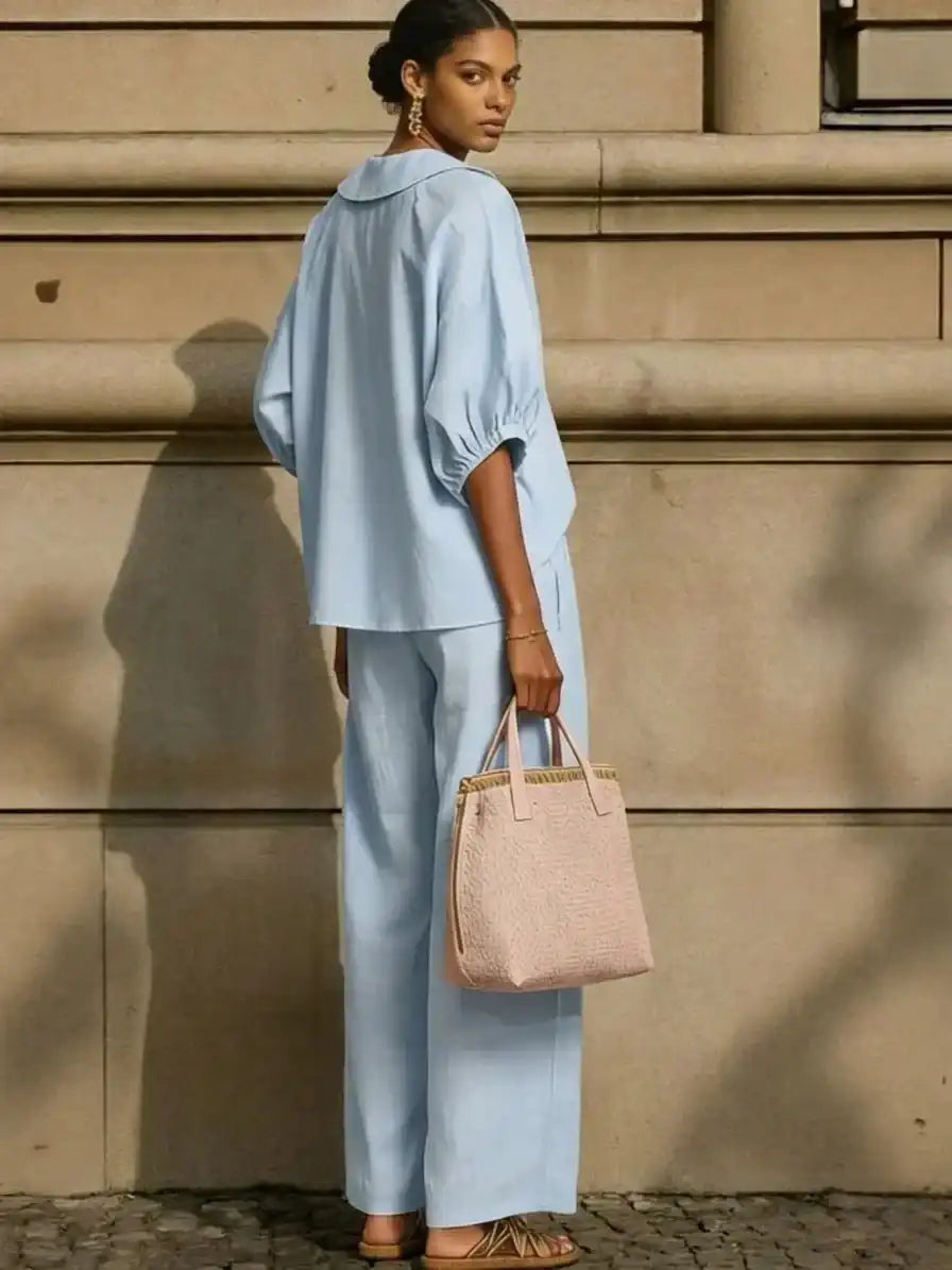 Woman in light blue relaxed fit blouse and wide-leg pants, holding pink woven tote, stylish plus size outfit