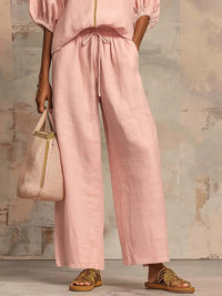 Pink wide-leg linen pants with drawstring waist, paired with matching top and woven sandals for relaxed style